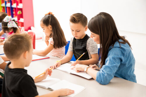 preschool teacher explaining writing assigment one her pupils classroom scaled